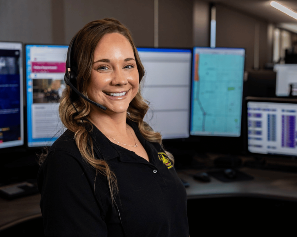 A 911 call-taker wearing a headset seated at a dispatch workstation in an emergency communications center, news photography style