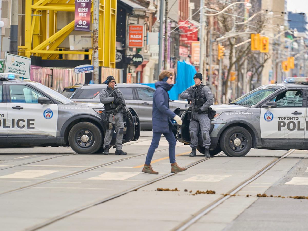 A Canadian police officer standing near an unmarked vehicle outside a downtown Toronto office building during an apparent security operation, news photography style