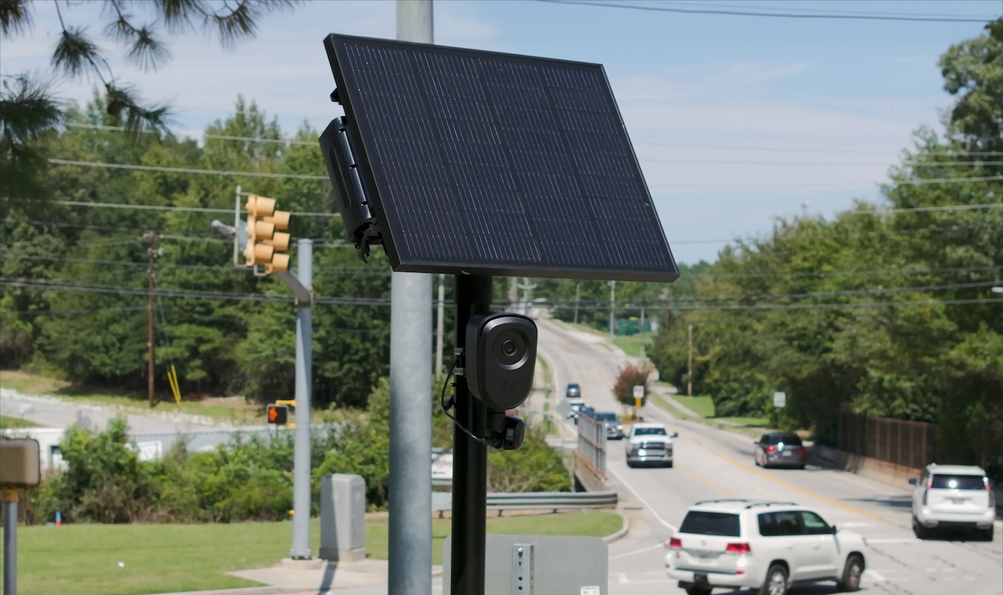 A Flock Safety automated license plate reader camera mounted on a pole above a city street in daylight