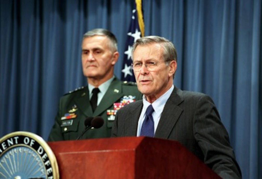 A Pentagon press briefing room during a wartime update, with a podium and seated journalists in a real indoor setting, news photography style