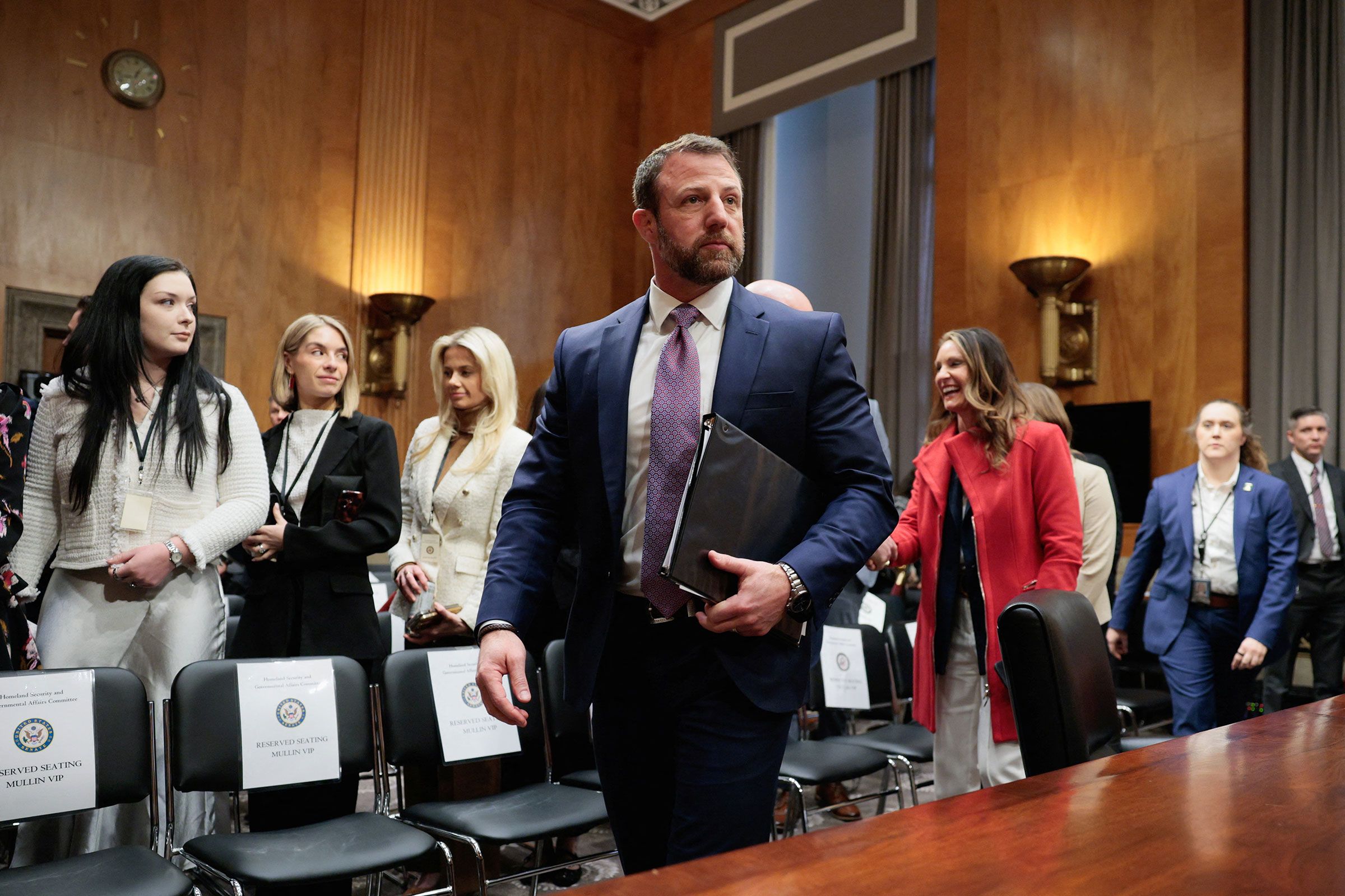 A Senate committee staffer walking through Capitol Hill hallways carrying binders and folders on a busy weekday, news photography style