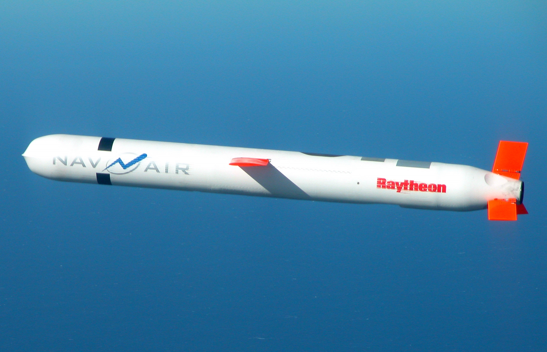 A Tomahawk cruise missile in flight over the ocean with a clear sky, captured in a sharp news-style photograph