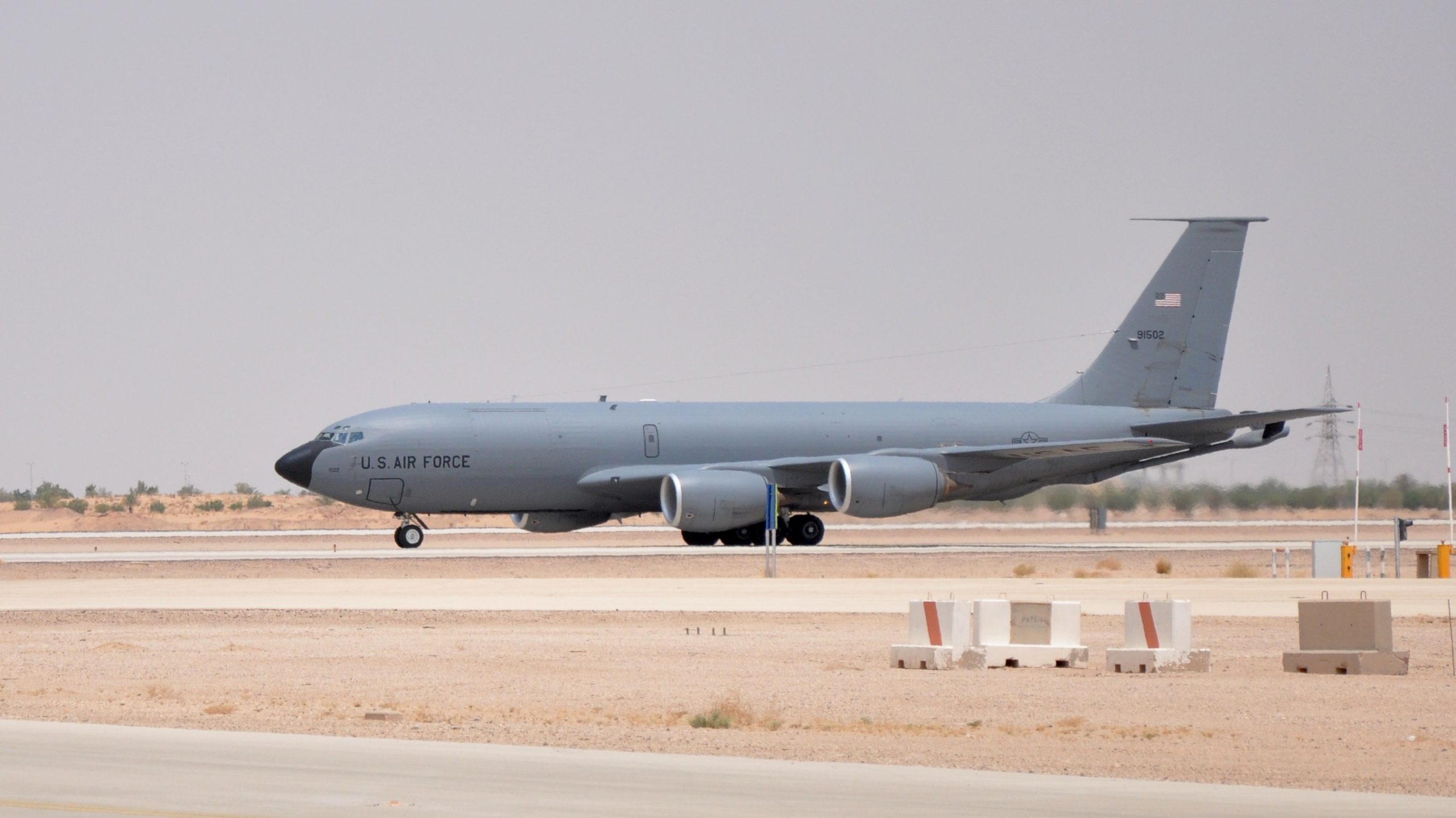 A U.S. Air Force KC-135 tanker parked on a tarmac with visible blast damage as maintenance crews inspect the aircraft at Prince Sultan Air Base, realistic news photography style