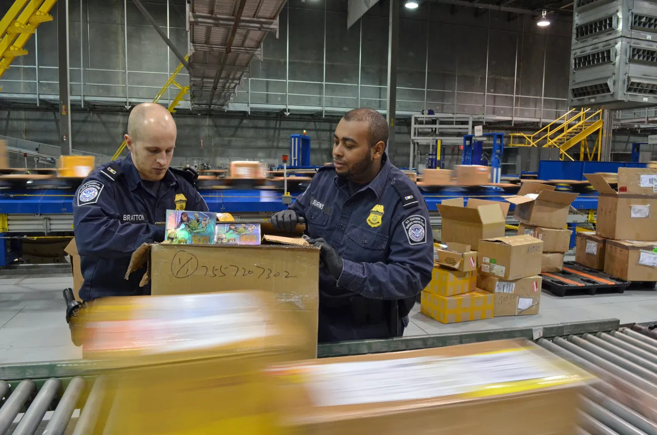A U.S. Customs and Border Protection officer inspecting imported packages at an international mail or express shipment facility