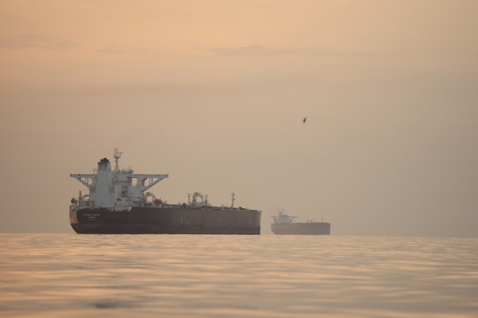 A U.S. Navy destroyer operating in the Strait of Hormuz during daylight, with an Iranian-flagged cargo ship in the distance on open water, news photography style