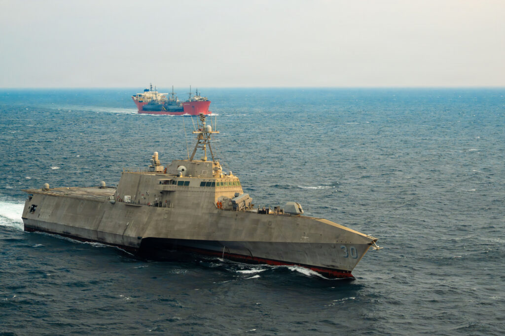 A U.S. Navy warship transiting the Strait of Hormuz in daylight with open water and distant coastline visible