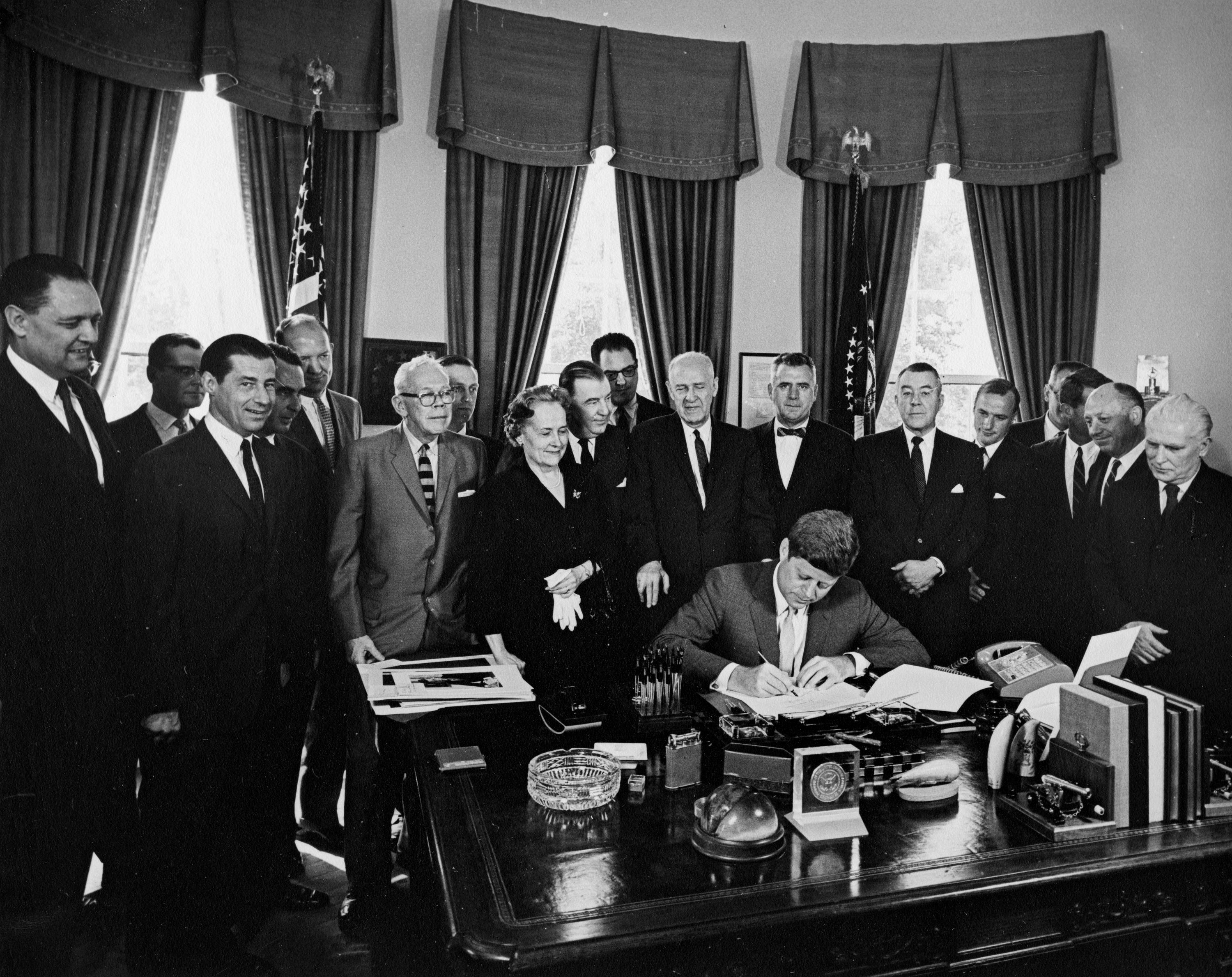 A U.S. President at a desk signing federal legislation in Washington, D.C., with lawmakers standing behind, news photography style