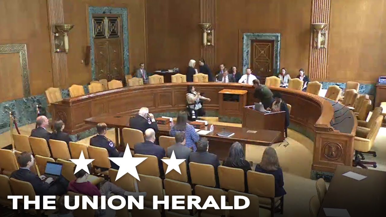 A U.S. Senate committee hearing room during a confirmation hearing, with senators seated at a dais and a nominee at a witness table under bright television lights, news photography style