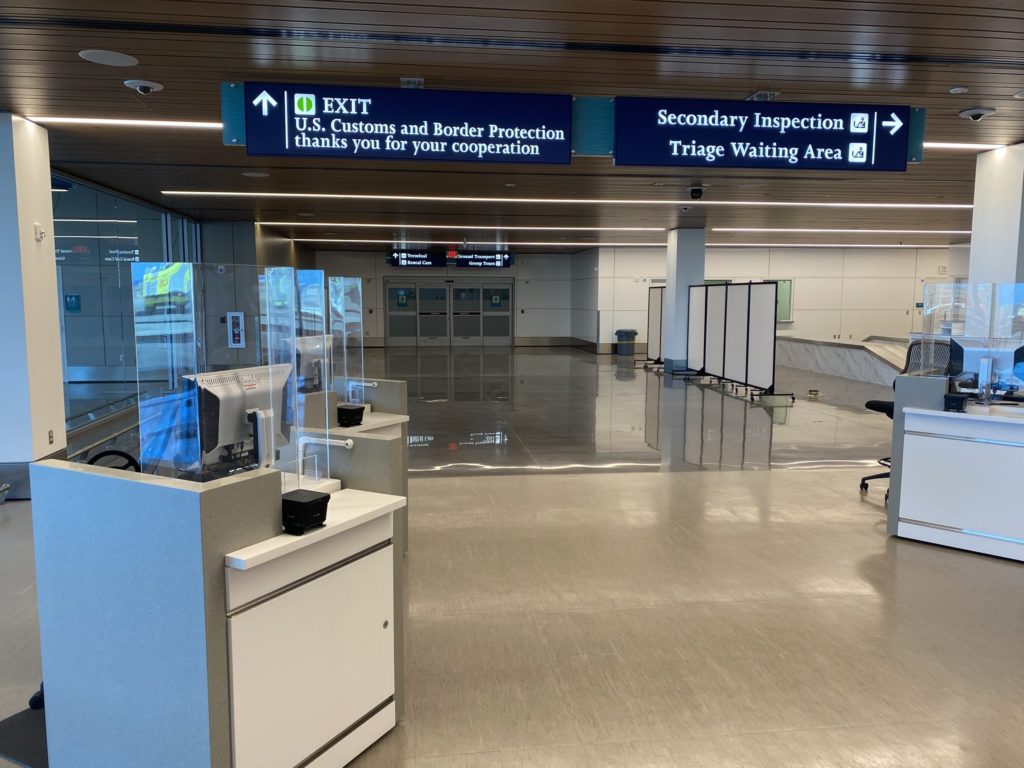 A U.S. airport secondary inspection area where travelers sit with luggage while CBP officers conduct additional screening