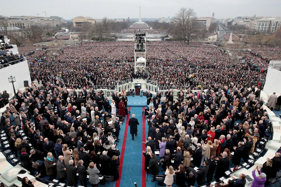 A U.S. president raising a right hand while taking the oath of office outdoors in Washington, D.C., with a chief justice holding a book and a crowd in the background, realistic news photo