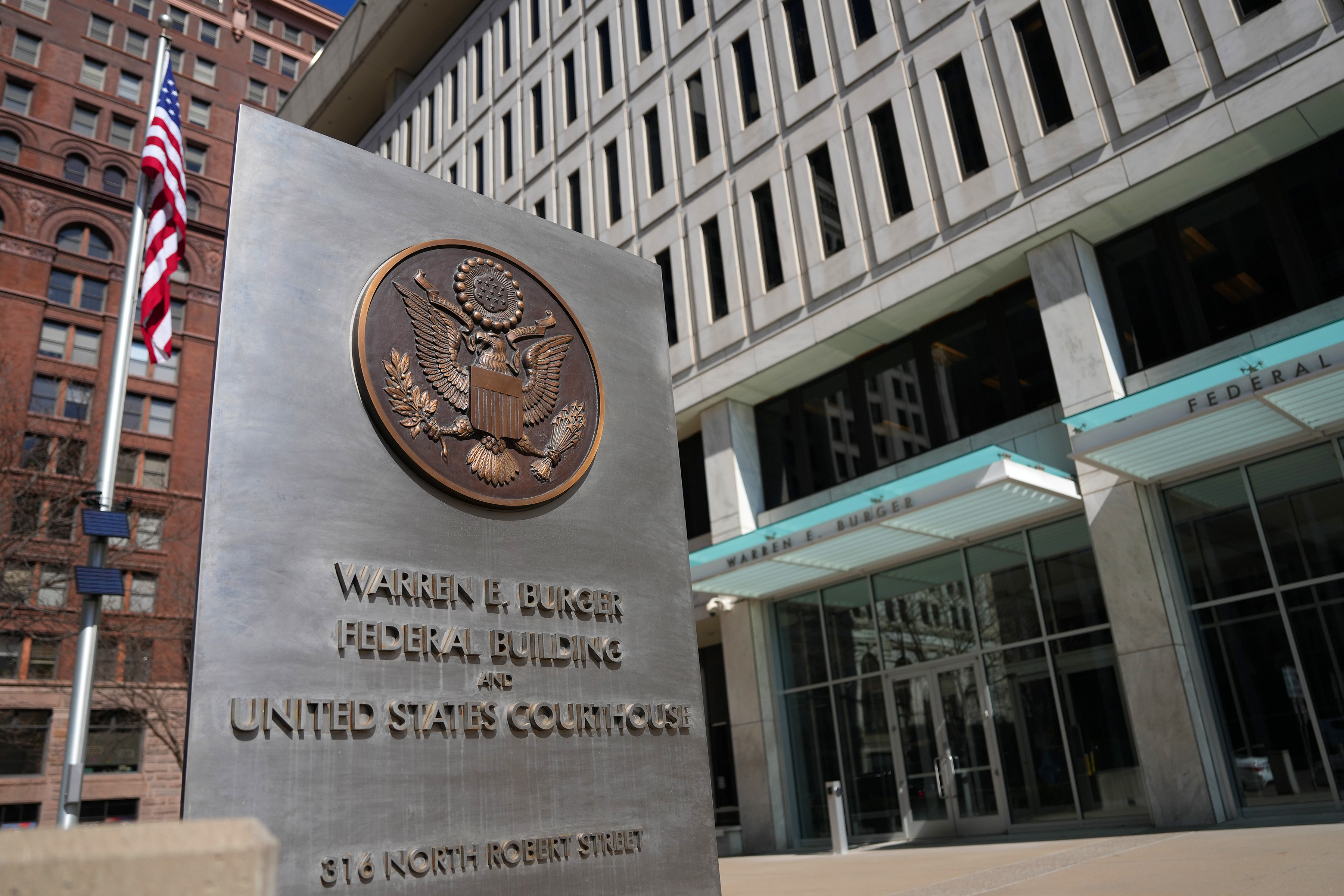 A United States Attorney office sign near the steps of a federal courthouse on a clear day, documentary news photography style