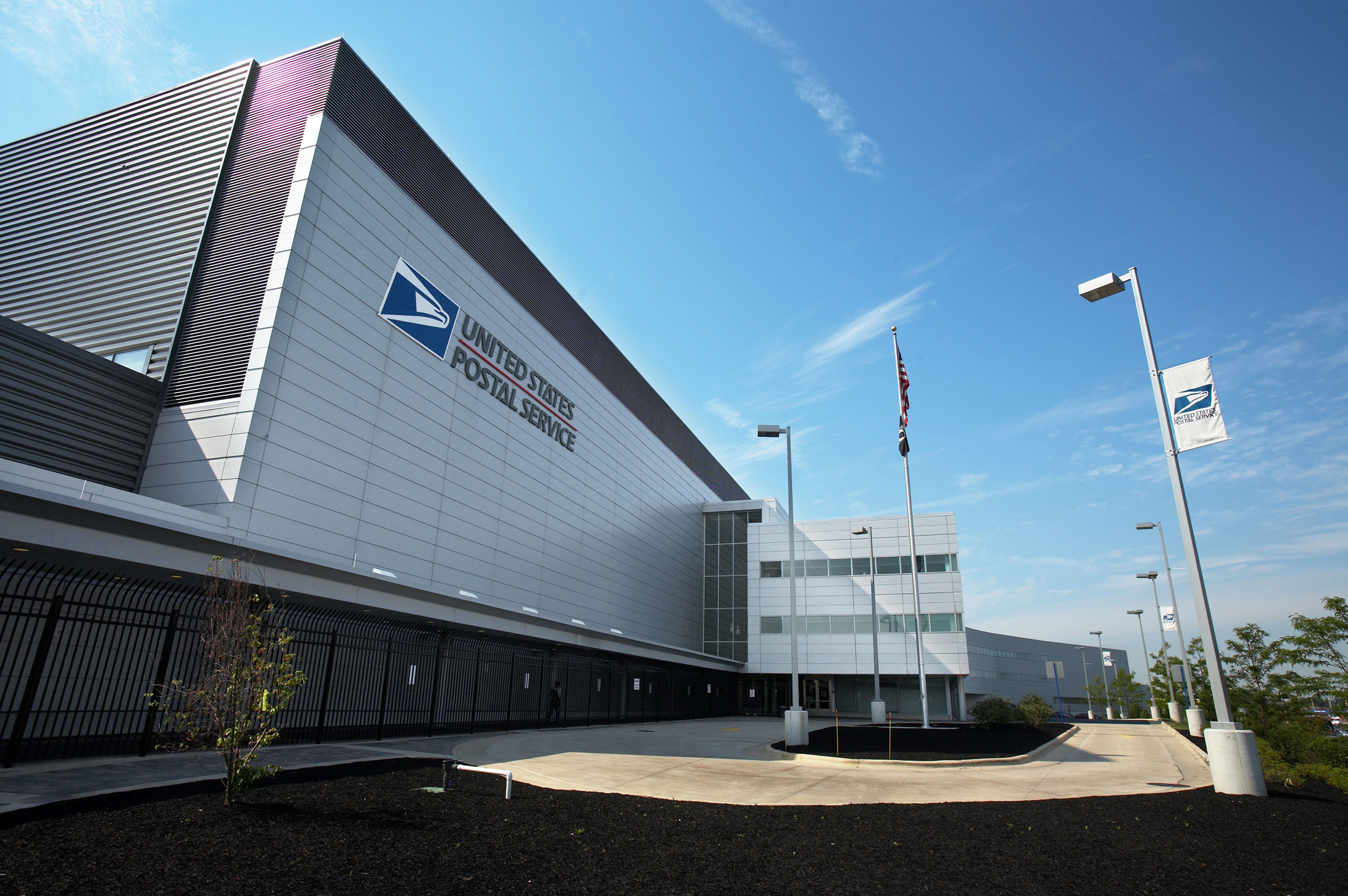 A United States Postal Service sign and building exterior in a public-facing setting