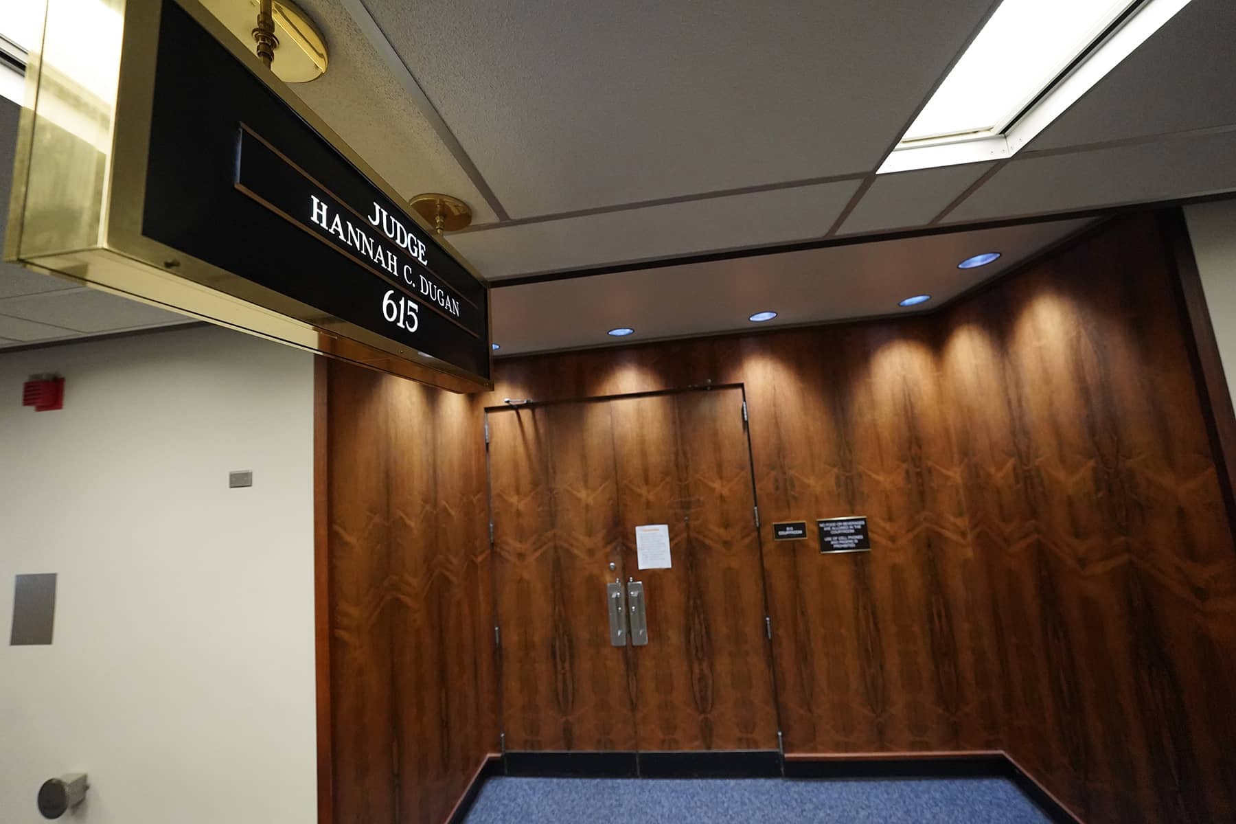 A candid photograph inside a county courthouse hallway with defendants, attorneys, and families waiting near courtroom doors during a busy criminal docket
