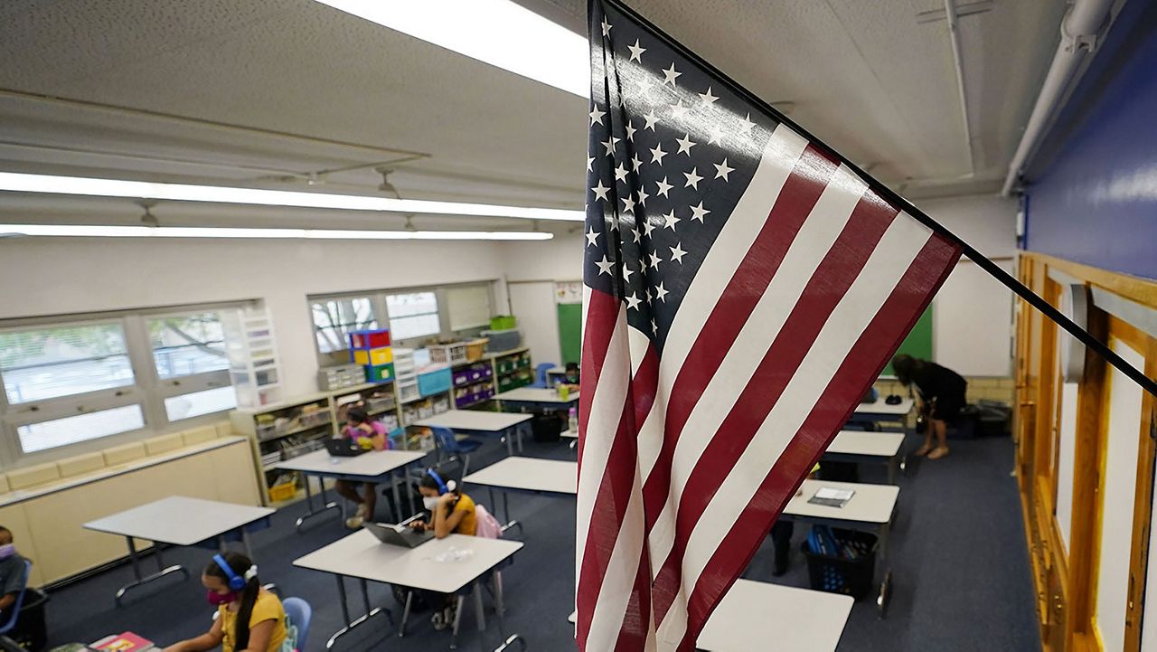 A classroom American flag mounted near a whiteboard in a Michigan public school classroom, empty desks, morning light, realistic news photography style