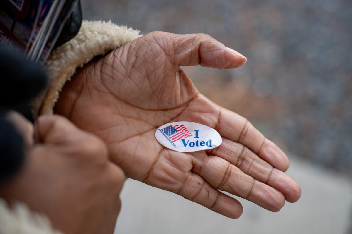 A close-up of a voter’s hand holding an I Voted sticker on election day in November 2022, natural light news photography style