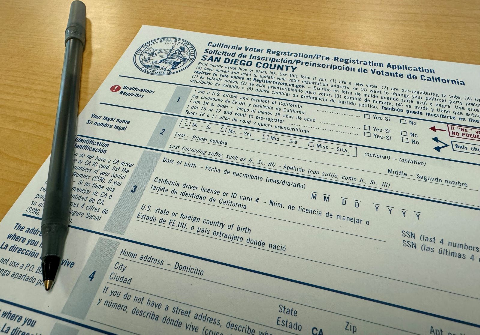 A close-up photograph of a voter registration form on a desk with a pen resting beside it, shot in natural light like a news photo