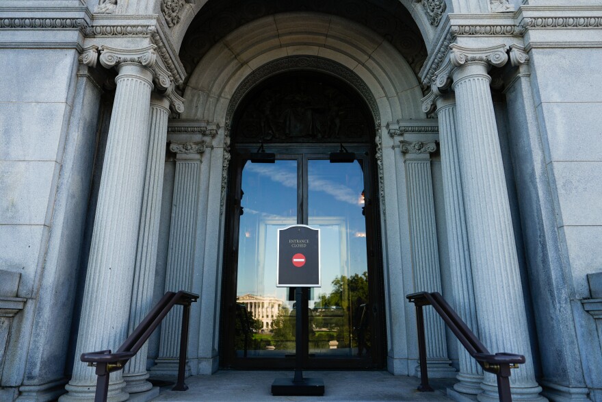 A closed entrance to a federal office building with locked glass doors and a posted notice, documentary news photo style