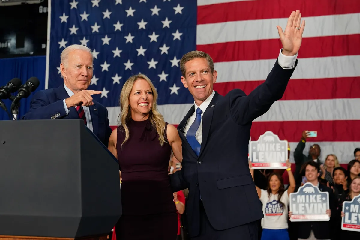 A congressional candidate speaking to a small crowd at an outdoor campaign event in the United States during a midterm year, with supporters listening, news photography style