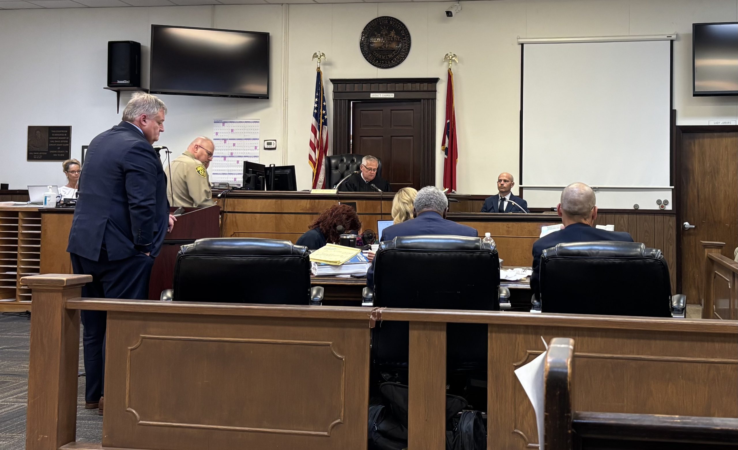A county criminal courtroom during a morning arraignment calendar, with the judge seated at the bench and attorneys standing at counsel tables, news photography style