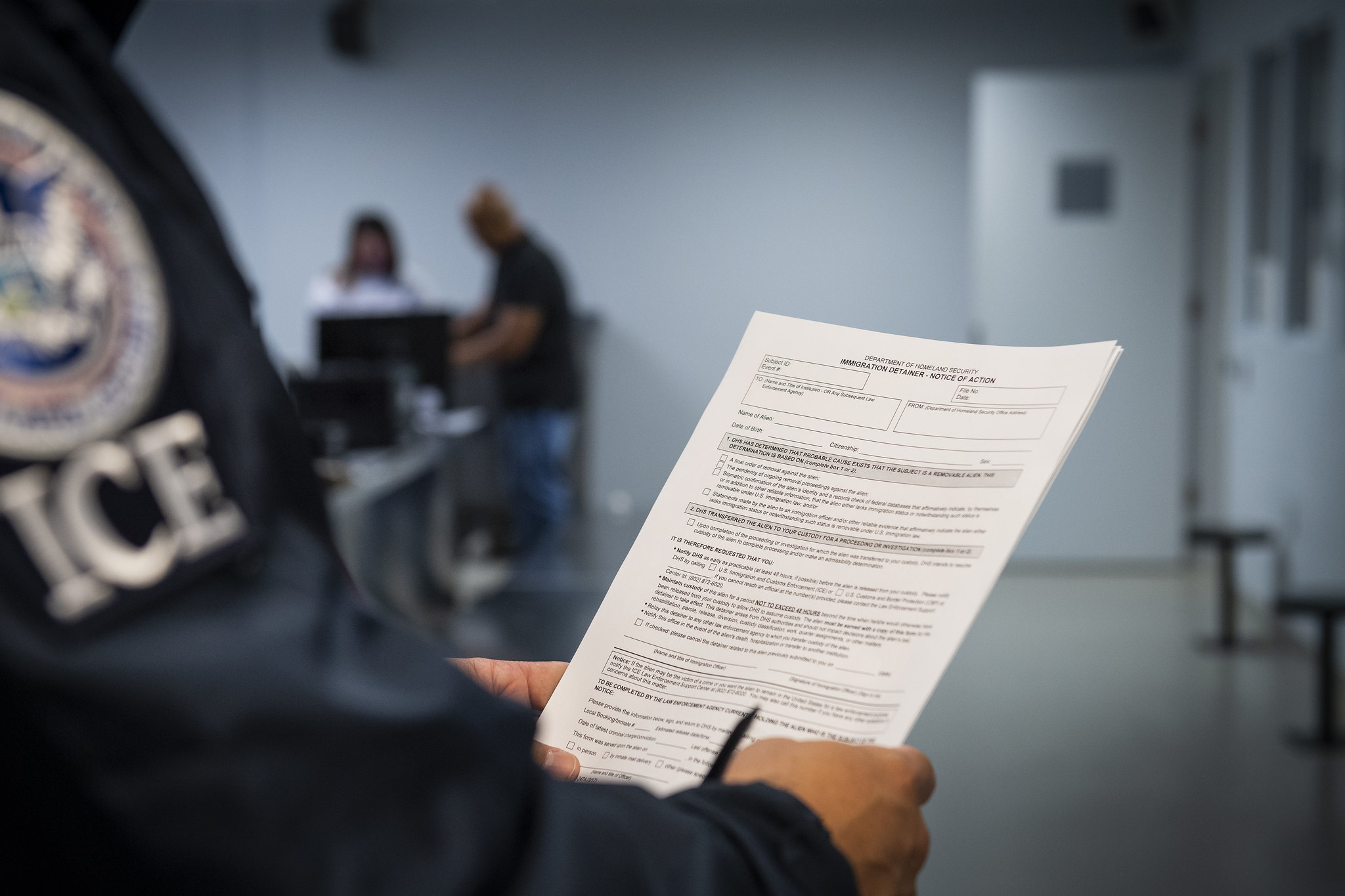 A county jail booking desk with an officer reviewing an ICE detainer request form next to a detainee file, documentary news photography style