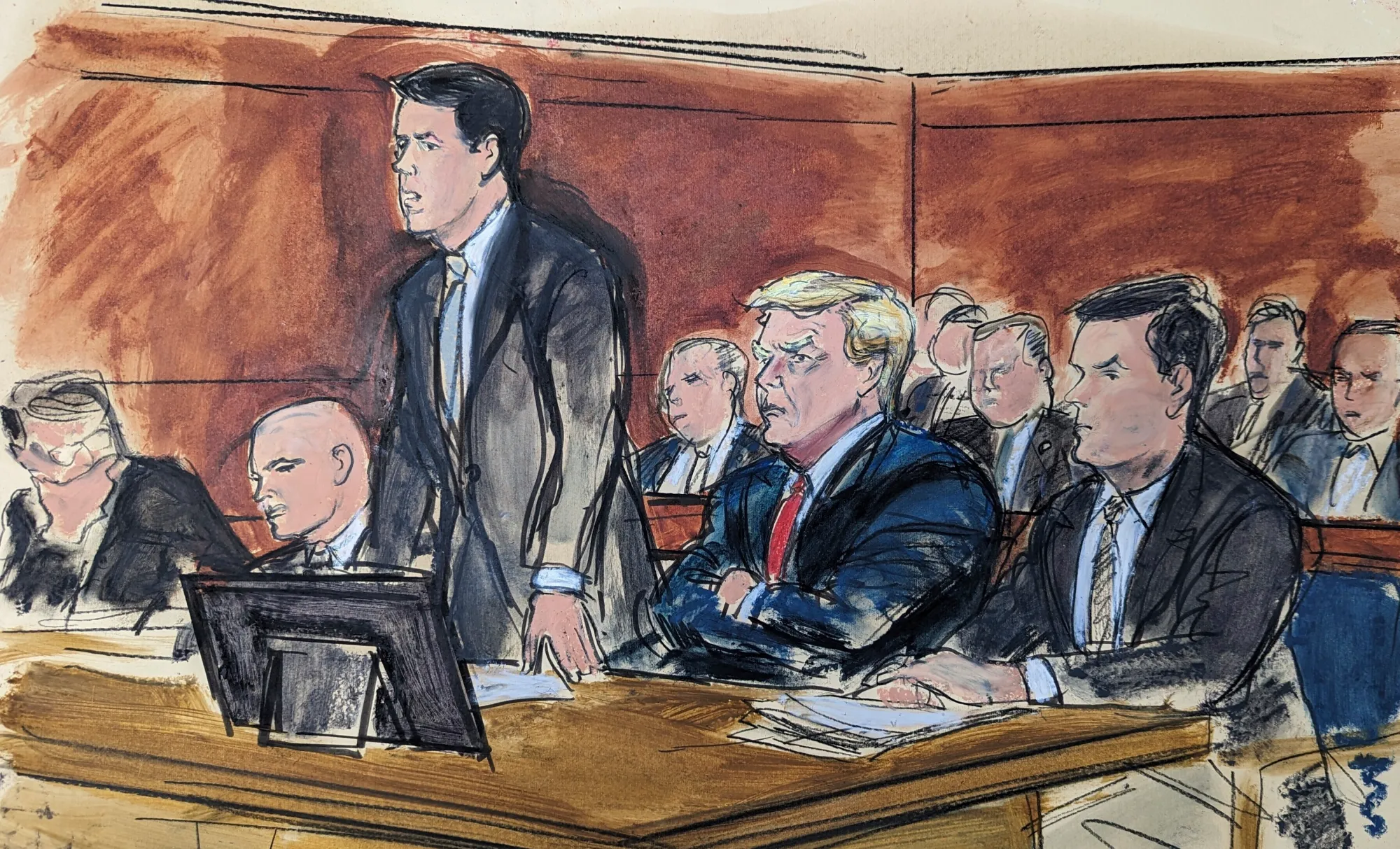 A courtroom sketch artist seated in the gallery drawing a judge and attorneys at counsel table during a busy hearing, real documentary photography style