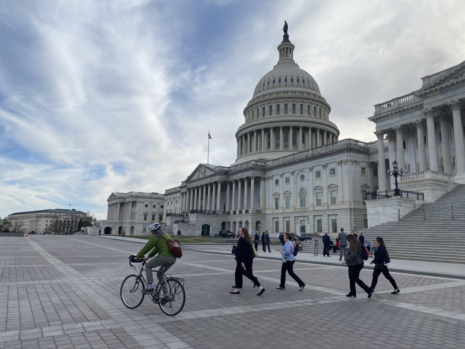 A crisp daylight photograph of the United States Capitol building in Washington, D.C., with the dome centered and people walking on the grounds in the mid-distance, representing congressional authority and national governance