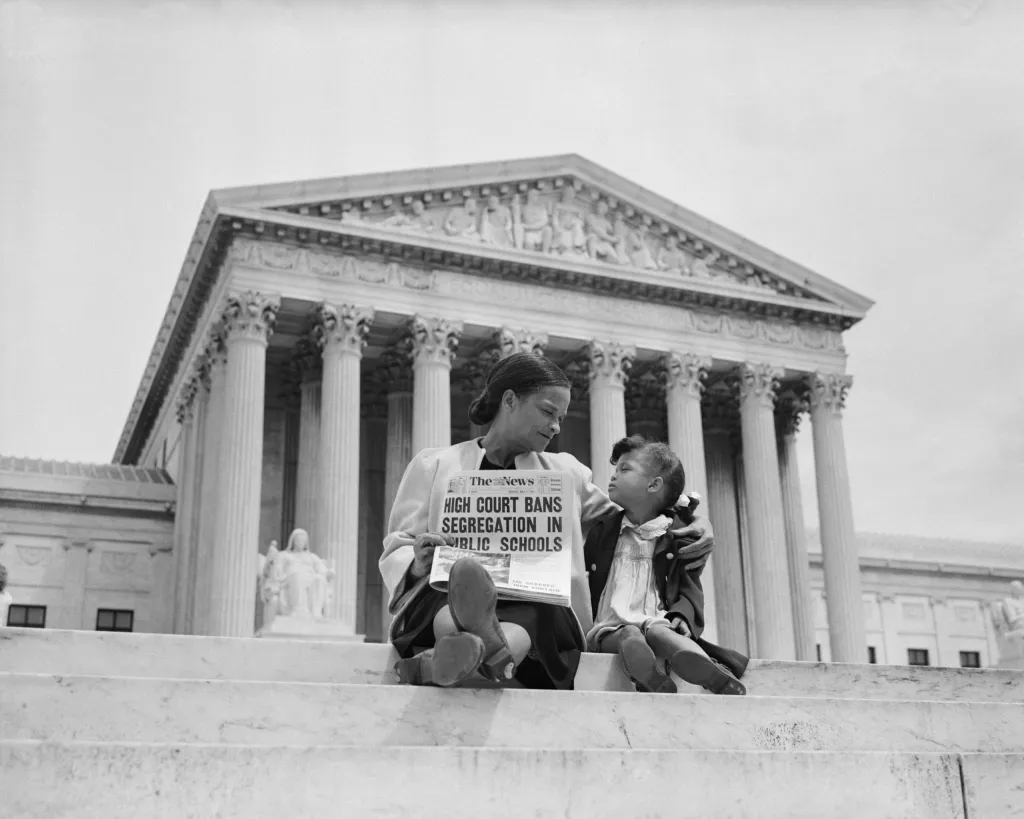 A crowd gathered on the steps outside the United States Supreme Court in 1954, with people holding papers and talking in small groups, news photography style