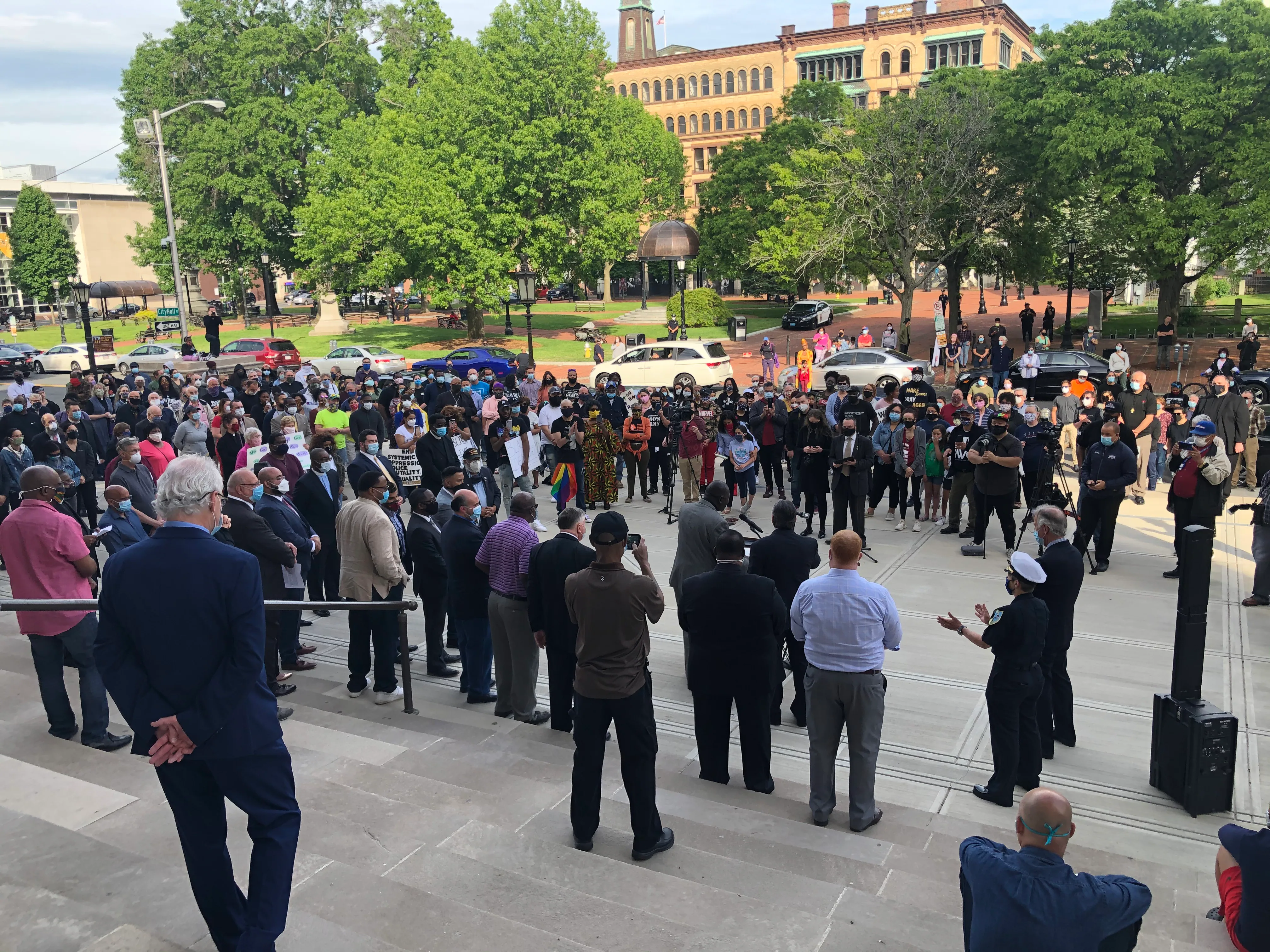 A crowd gathers in the stone courtyard outside Springfield City Hall at dusk, holding signs in support of Haitian neighbors while speakers address the community