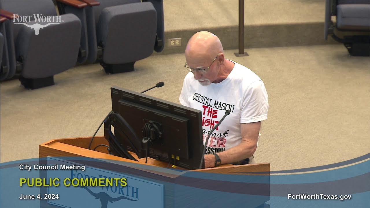 A crowded city council chamber during a public comment period, with a speaker standing at a podium and council members seated at a dais, news photography style