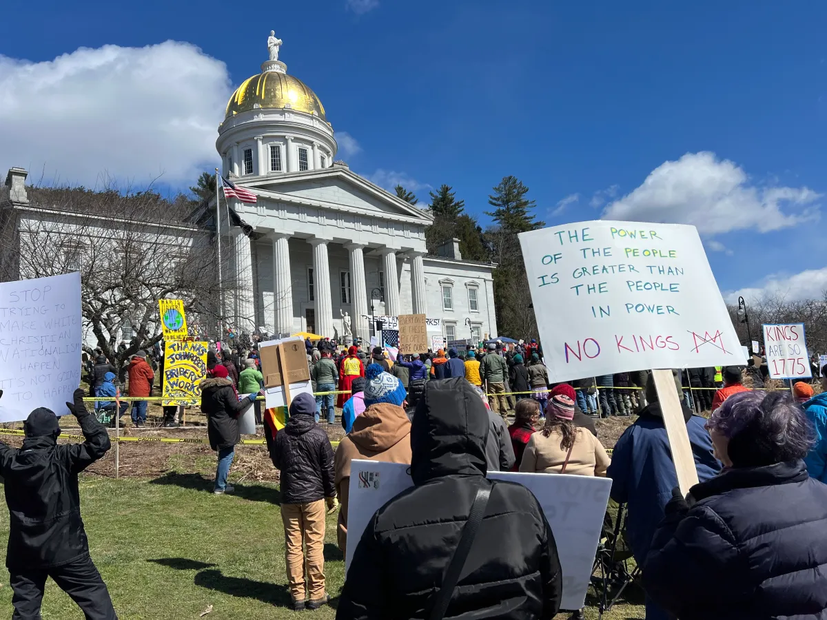 A daytime photograph of peaceful demonstrators holding signs near a government building, with police monitoring from a distance, news photography style