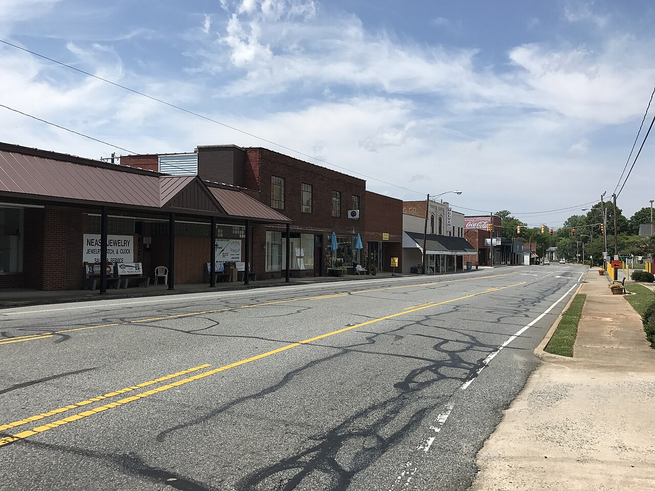 A daytime street-level photograph of downtown Randleman, North Carolina, with storefronts and passing cars, news photography style