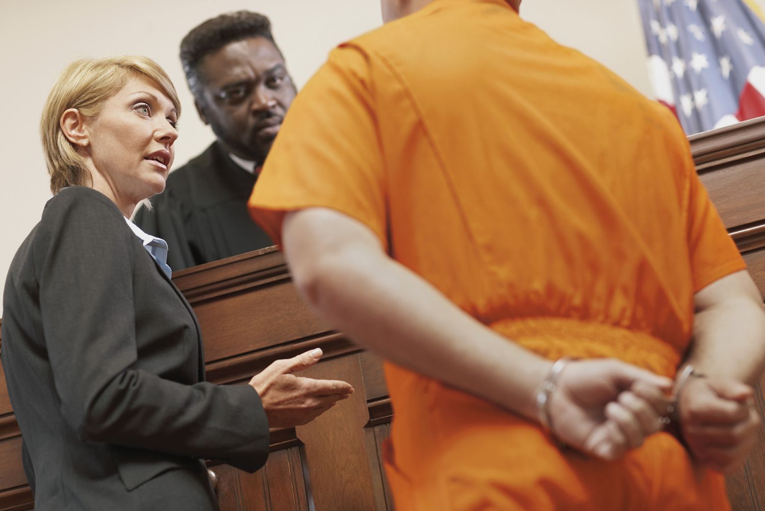 A defendant standing beside defense counsel at a courtroom lectern while a judge sits on the bench during a criminal arraignment, realistic news photography style