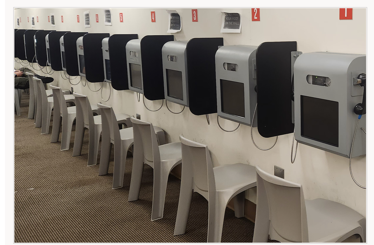 A defense attorney speaking with a client through glass in a county jail attorney visitation room, realistic news photography