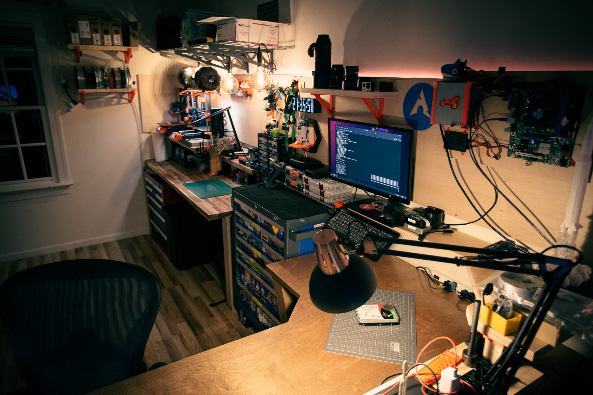 A desktop 3D printer operating on a workbench with a filament spool nearby.