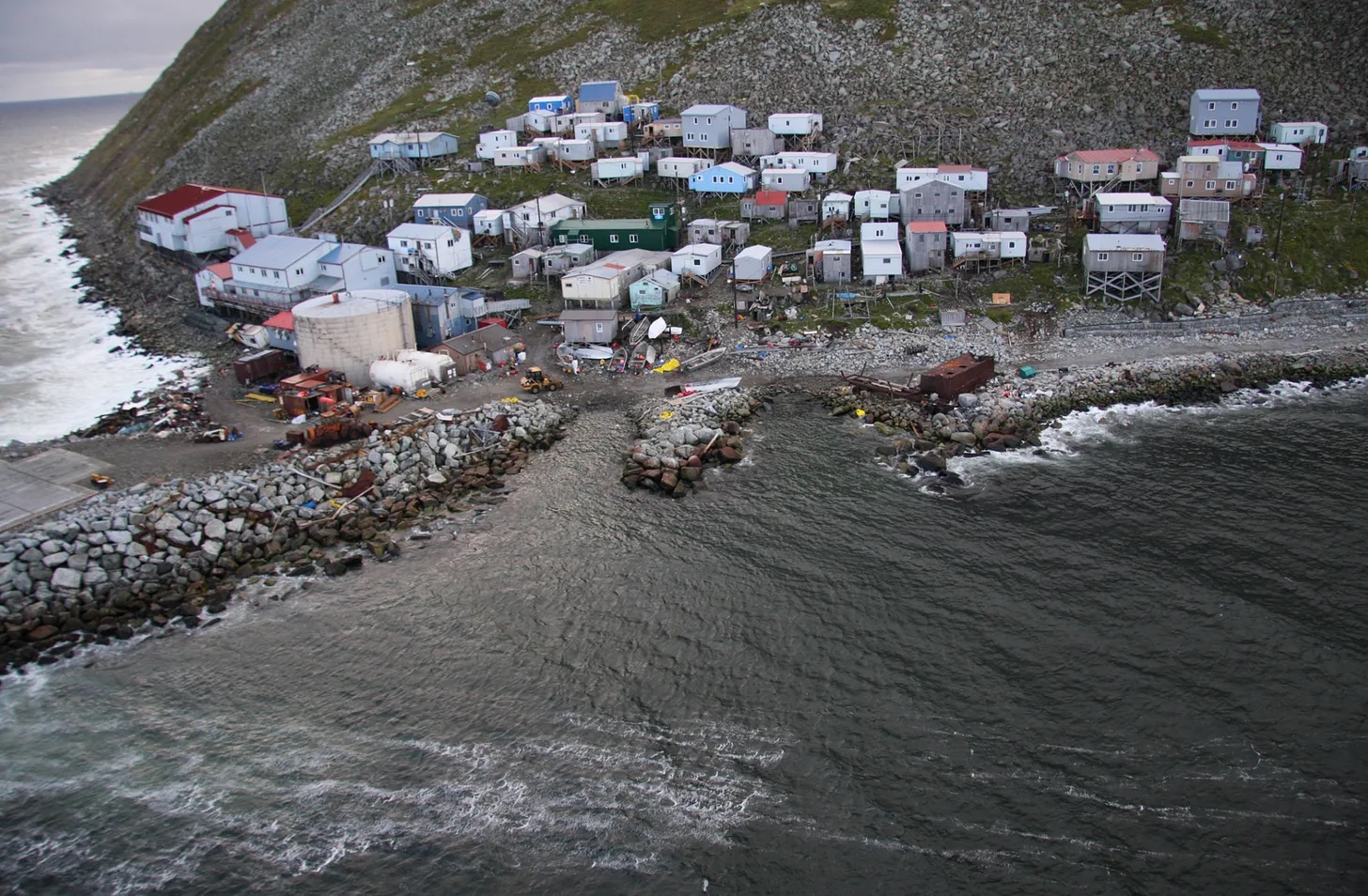 A documentary-style photograph of Platinum, Alaska, a small coastal community along the Bering Sea with clustered buildings near the shoreline