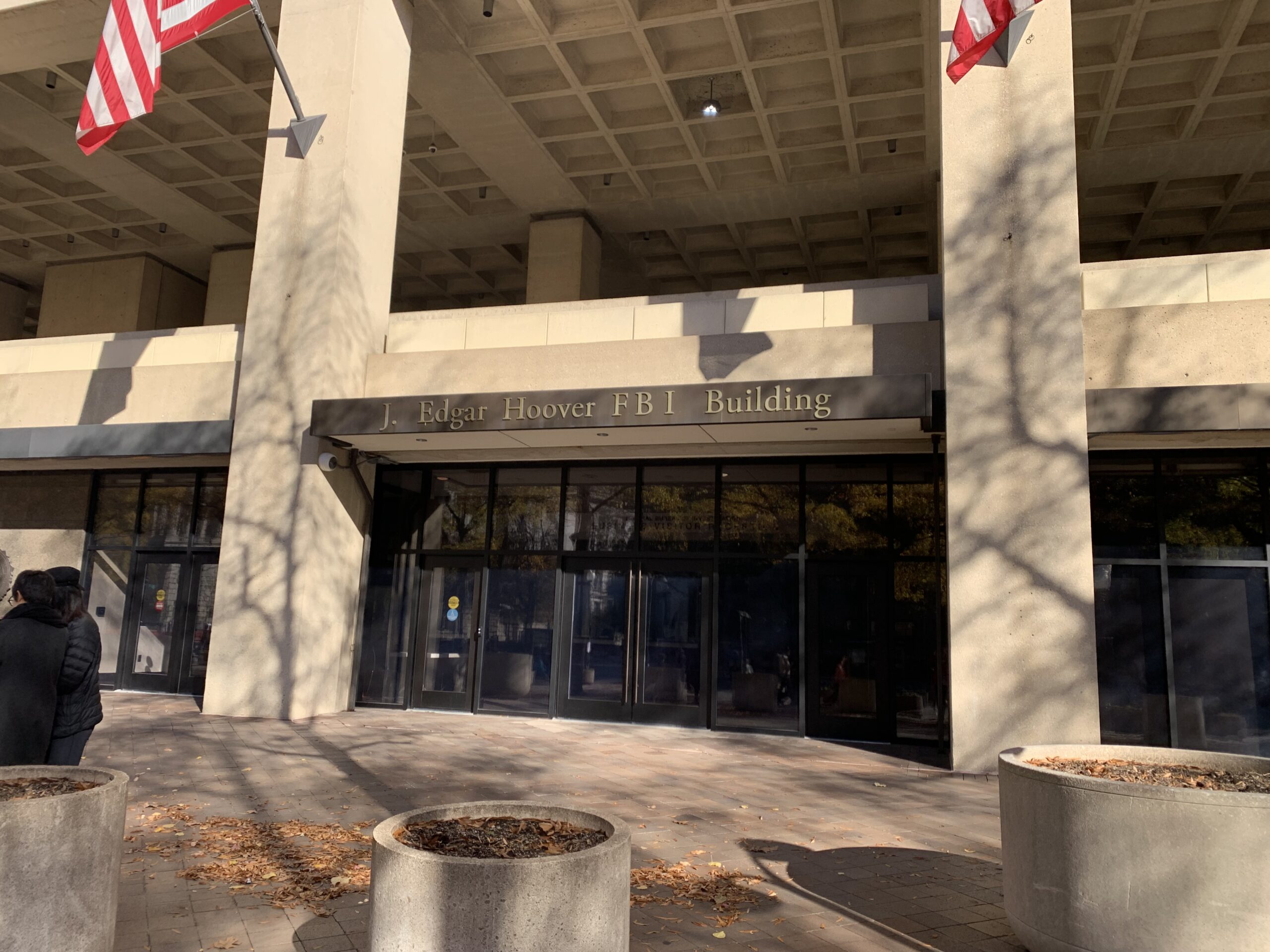 A federal administrative agency building entrance in Washington, DC with people walking through security on a weekday, realistic news photography style