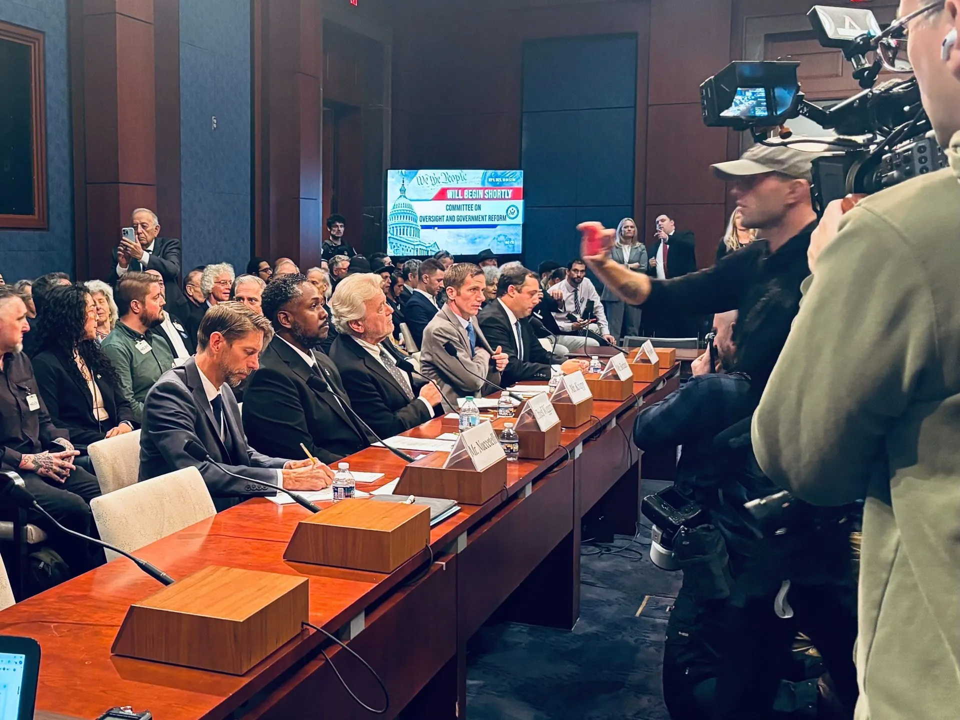 A federal civil deposition in a modern conference room, with a witness seated at a table next to counsel while a court reporter records testimony, documentary photo style
