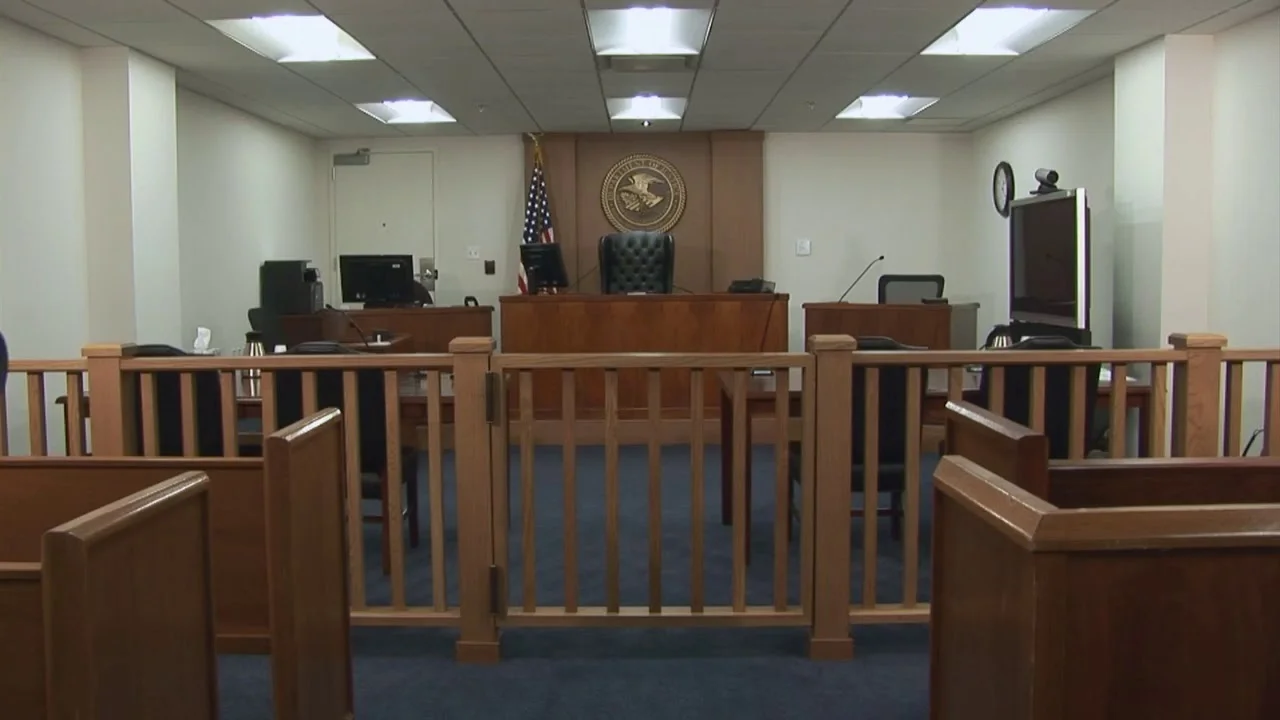 A federal courtroom scene with a judge seated at the bench and attorneys standing at counsel tables, formal lighting, serious mood, news photography style