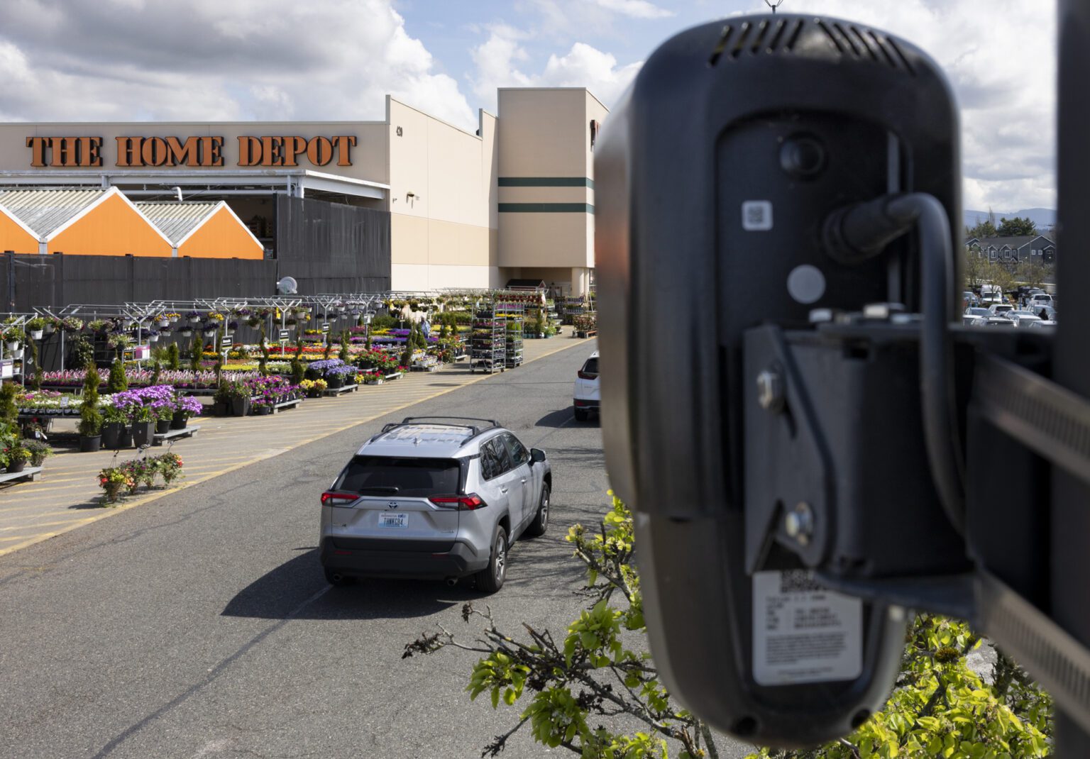 A fixed surveillance camera mounted on a utility pole overlooking a quiet residential street with single-family homes in the background, realistic news photography style