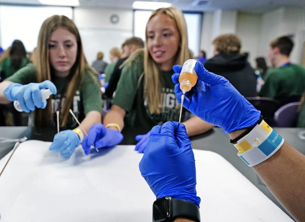 A forensic laboratory technician in a lab coat working at a bench with evidence containers and testing equipment in a crime lab, documentary photography style