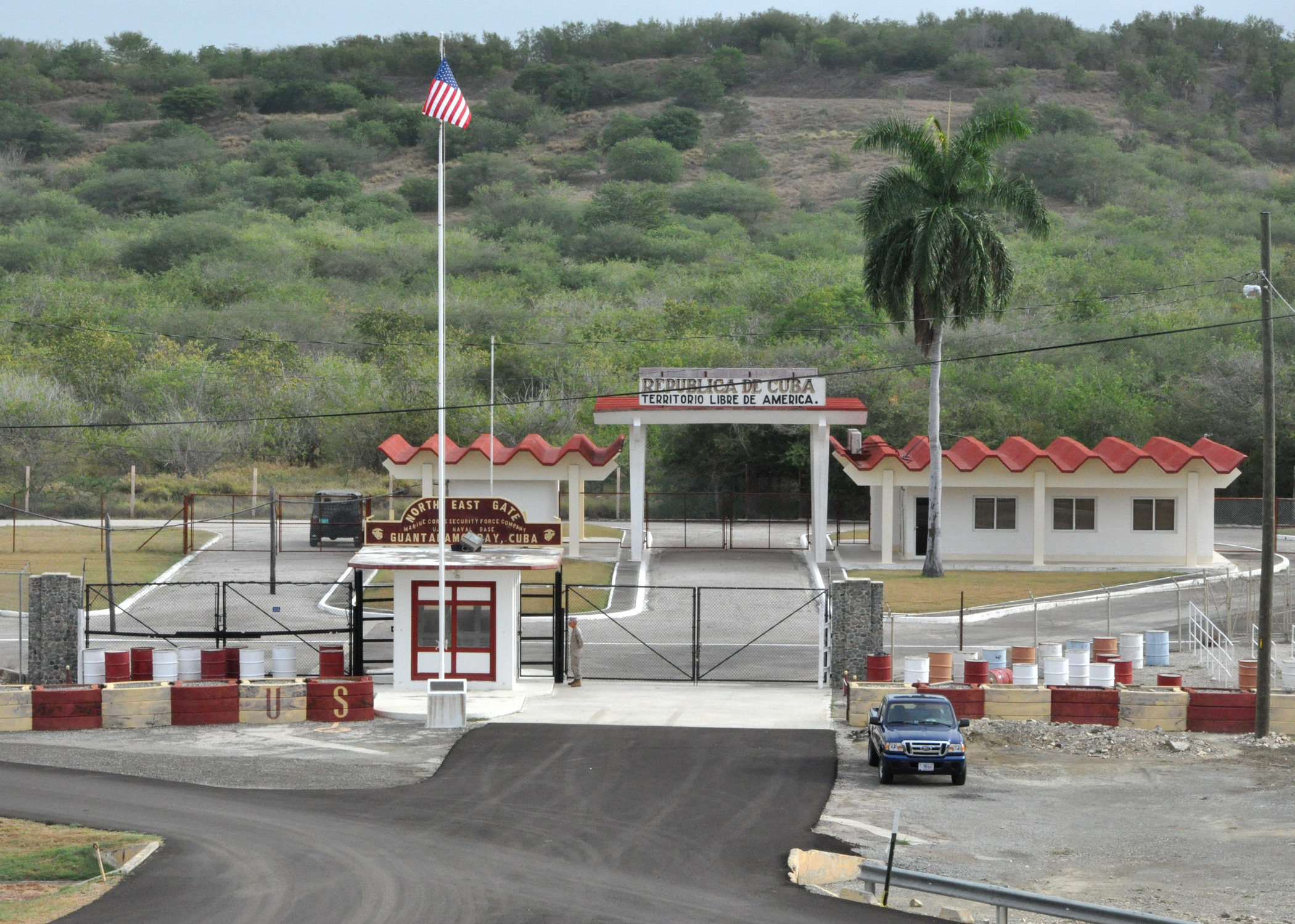 A guarded entrance area at Guantánamo Bay Naval Base in Cuba with fencing and a checkpoint, photographed in a realistic documentary style