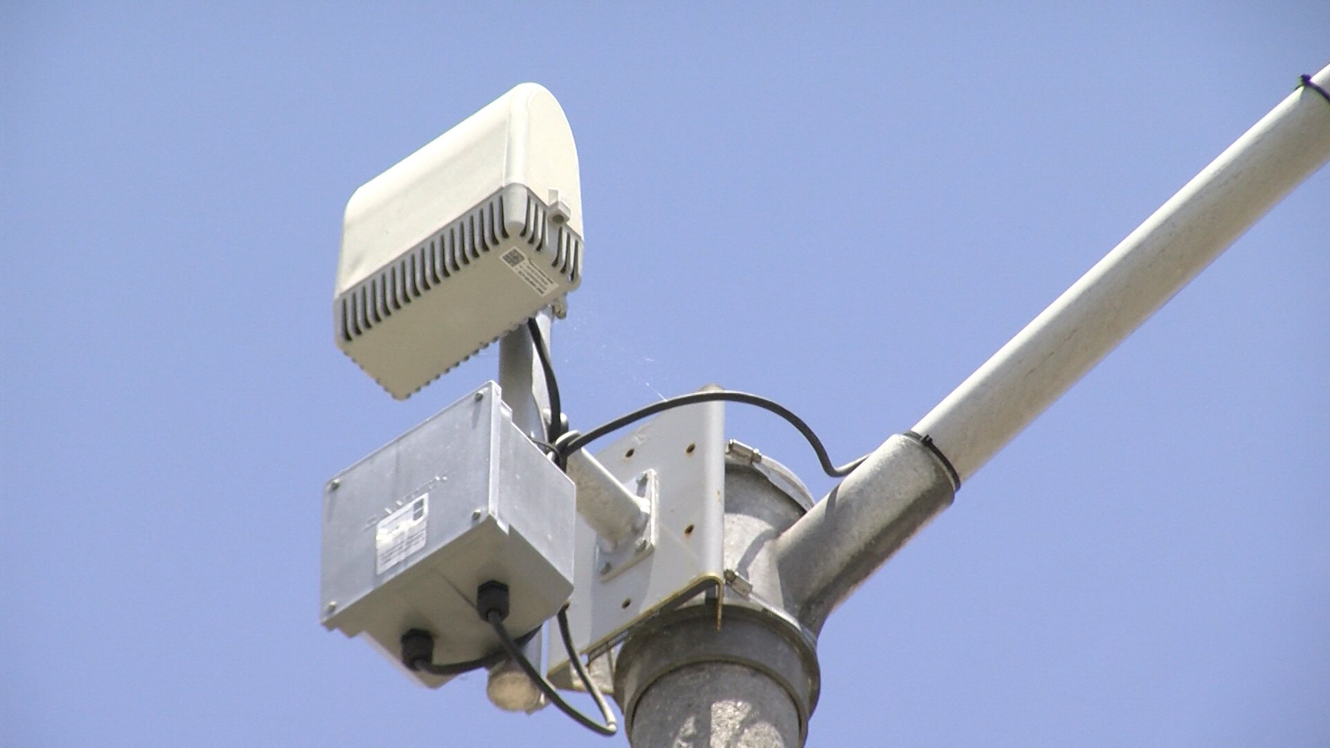 A gunshot-detection acoustic sensor mounted high on a utility pole in a city neighborhood