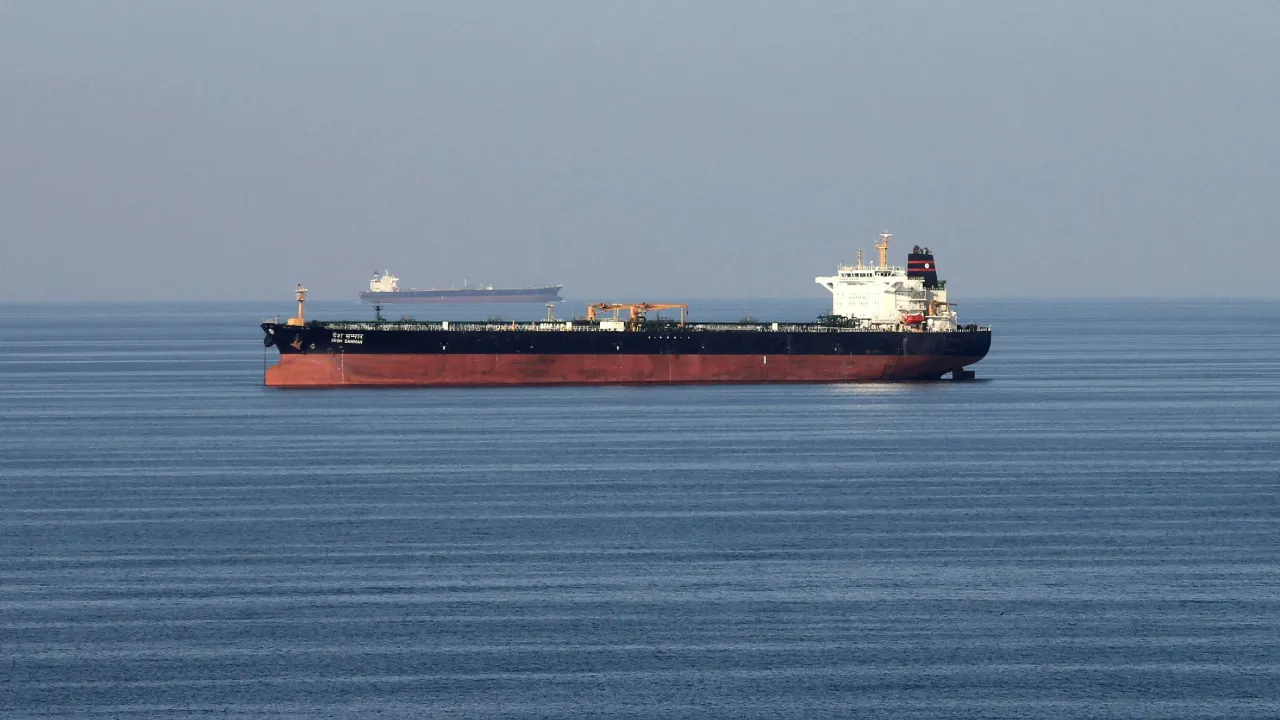 A large oil tanker transiting near the Strait of Hormuz in daylight, photographed from the water with escort vessels visible in the distance