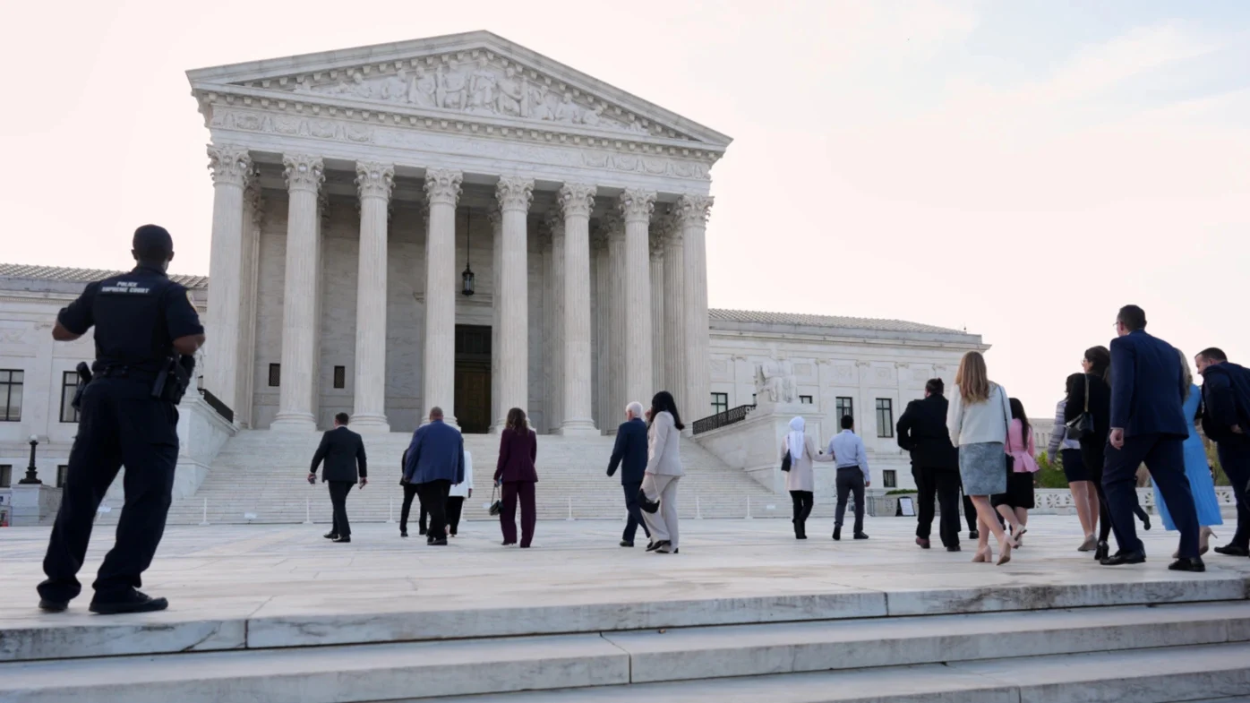 A lawyer in a dark suit carrying a briefcase walking up the steps toward the entrance of the United States Supreme Court building on a clear morning