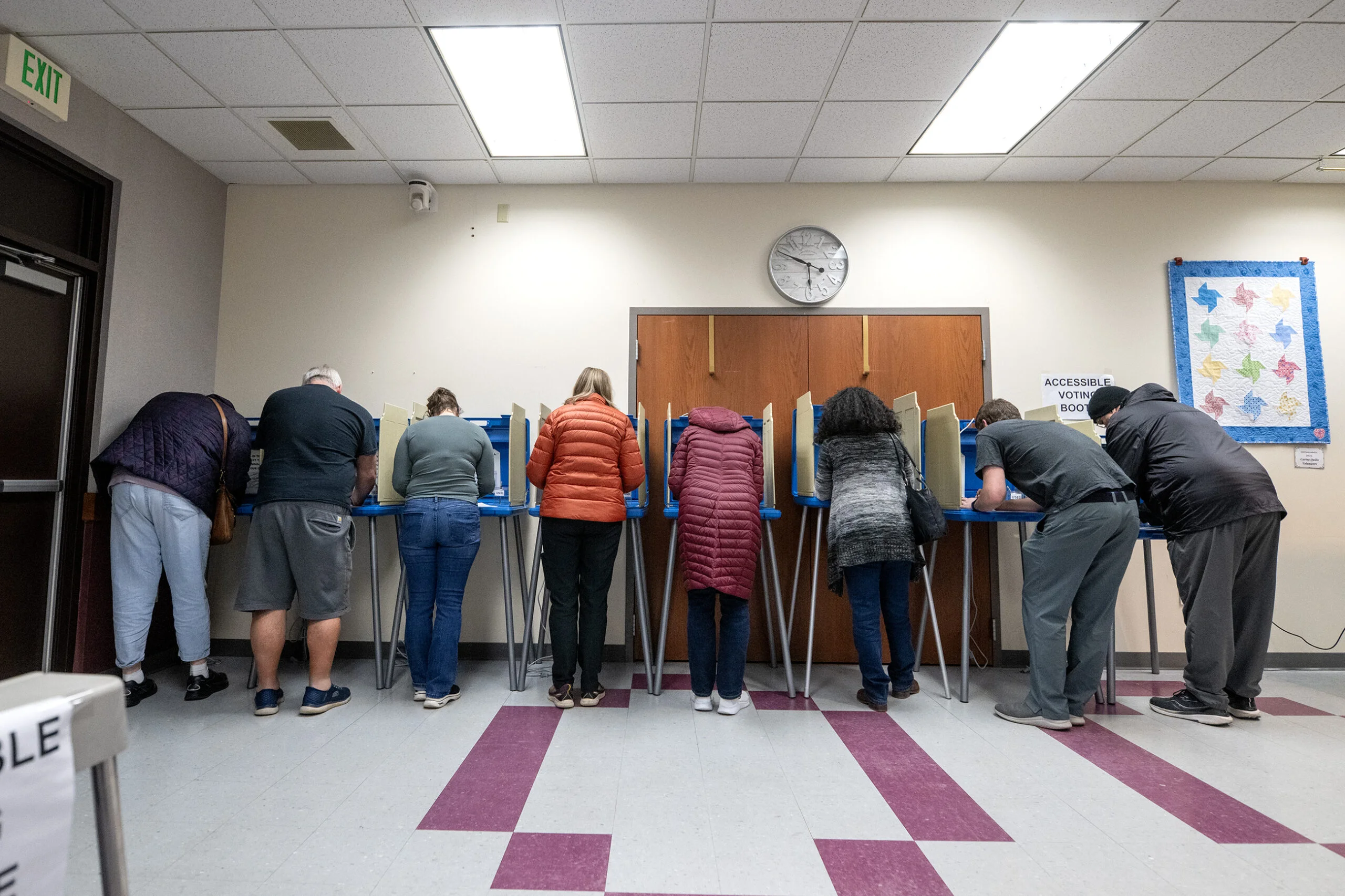 A line of American voters waiting outside a local polling place on a spring afternoon, with election workers visible near the entrance, news photography style