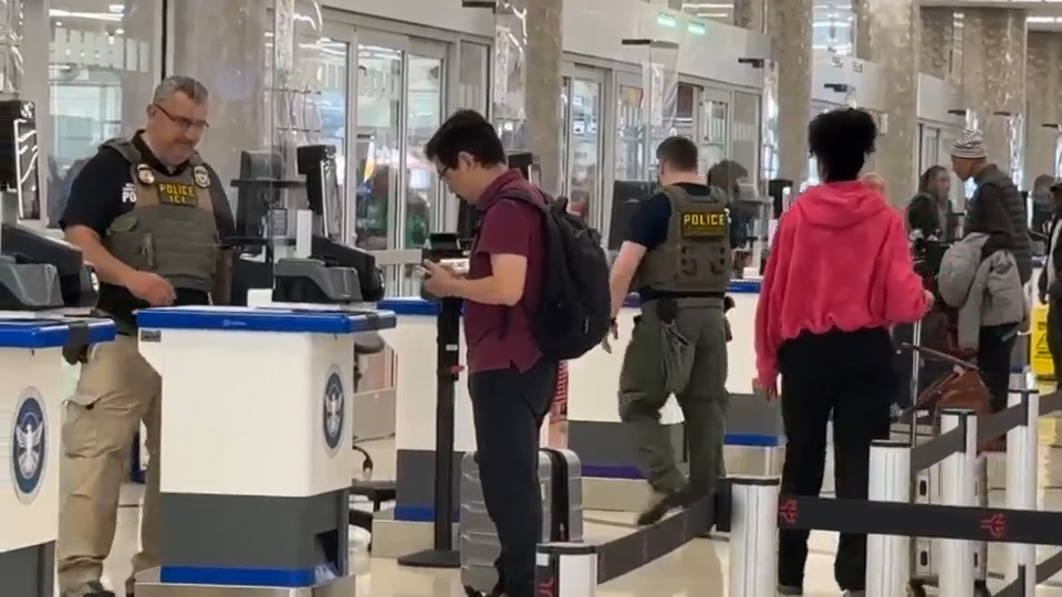 A line of people passing through security screening at the entrance of a federal courthouse, with metal detectors and court security officers visible