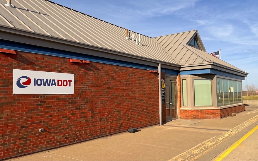 A line of semi trucks and cargo trailers passing a highway weigh station on an interstate route in the United States, daytime documentary photo