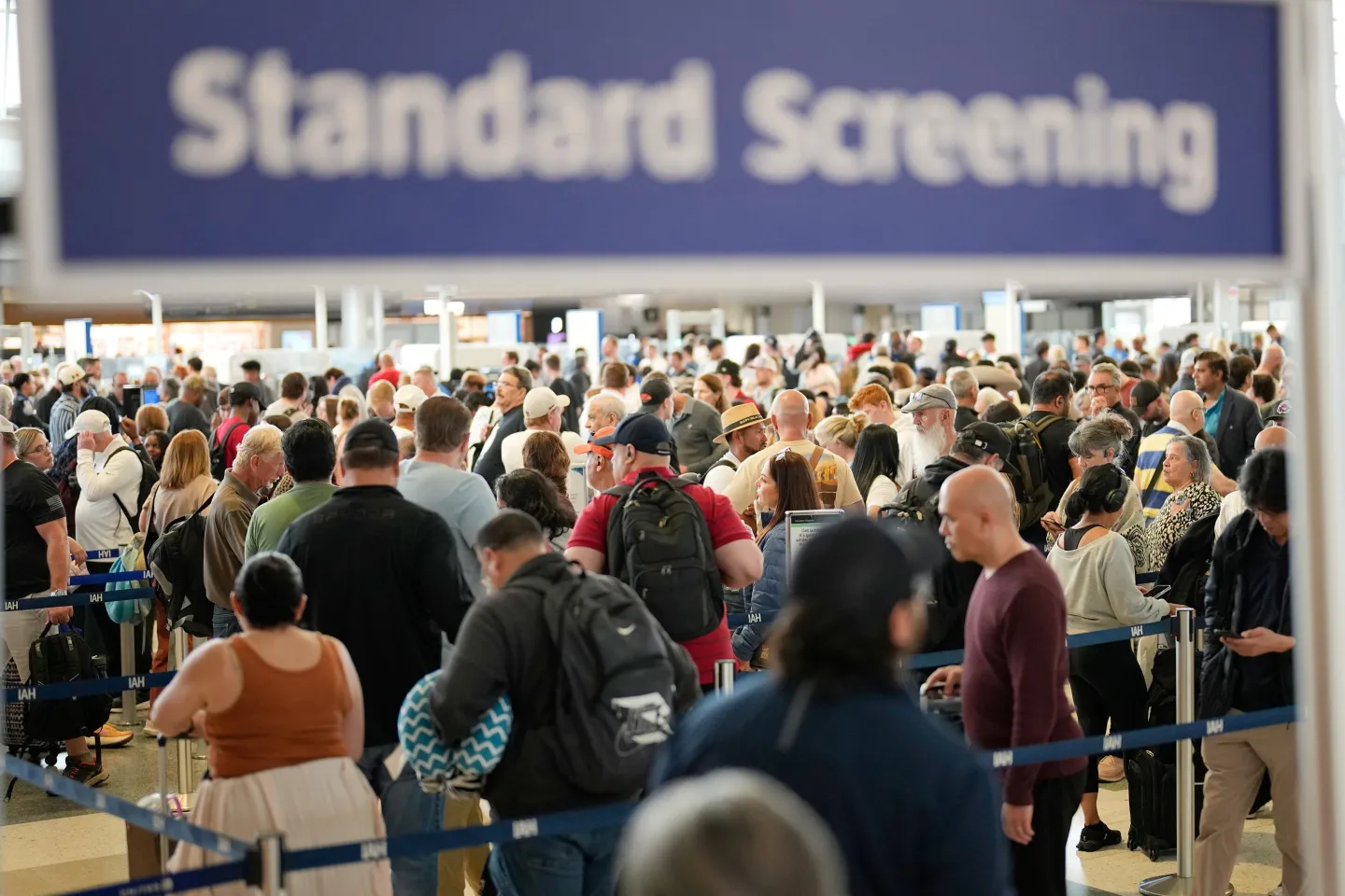 A long TSA security line inside a busy airport terminal with travelers waiting behind stanchions near the checkpoint, news photography style