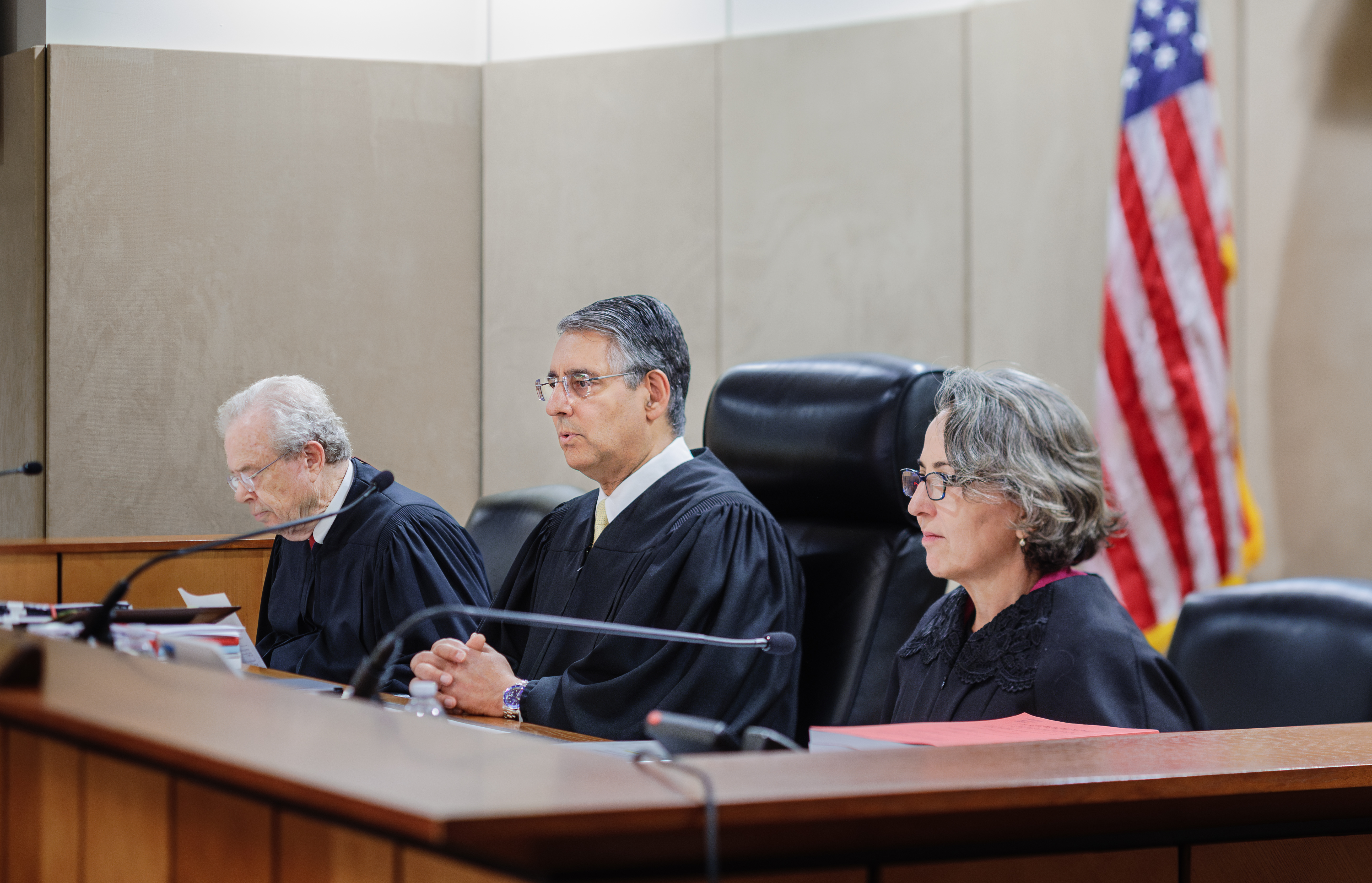 A magistrate judge seated in a federal courtroom with attorneys standing at counsel tables during an initial appearance hearing, realistic photojournalism style