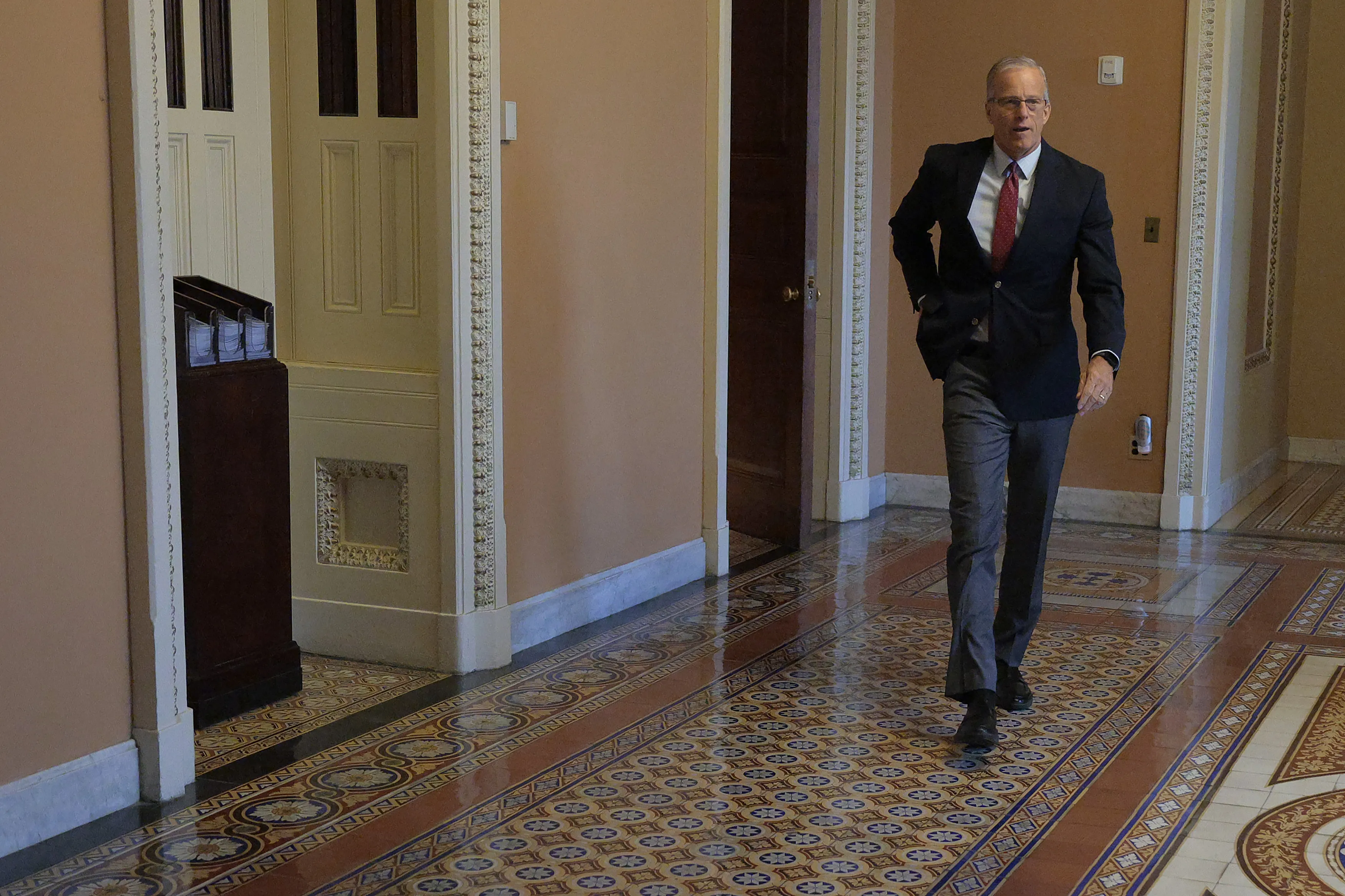 A marble hallway inside the United States Senate with a few senators and staff walking past the camera, candid news photography style